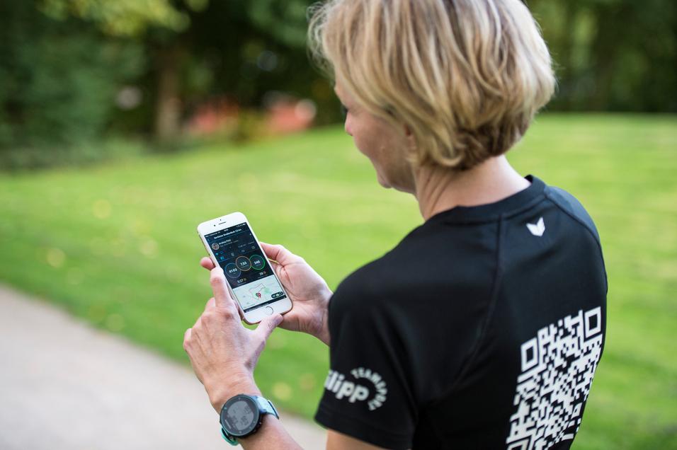 Frau mit kurzen Haaren schaut auf ein Smartphone, während sie auf einem Weg in einem Park steht.