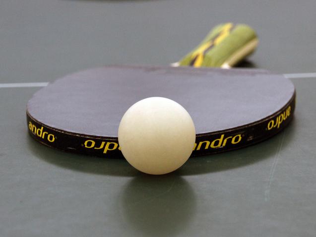 Nahaufnahme eines Tischtennisschlägers mit weißem Ball auf einer grünen Tischtennisplatte.